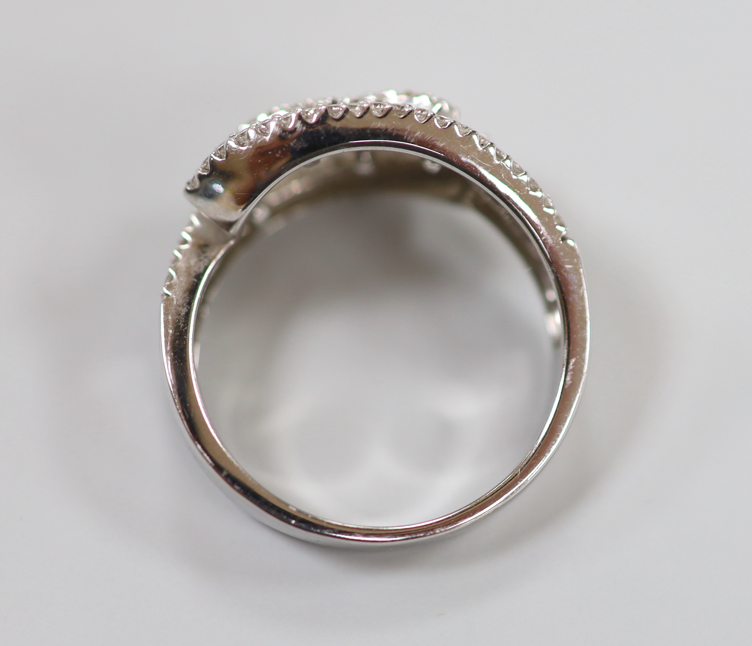 A modern 18ct white gold, baguette cut and diamond chip cluster set crossover ring, size O, gross weight 4.7 grams.